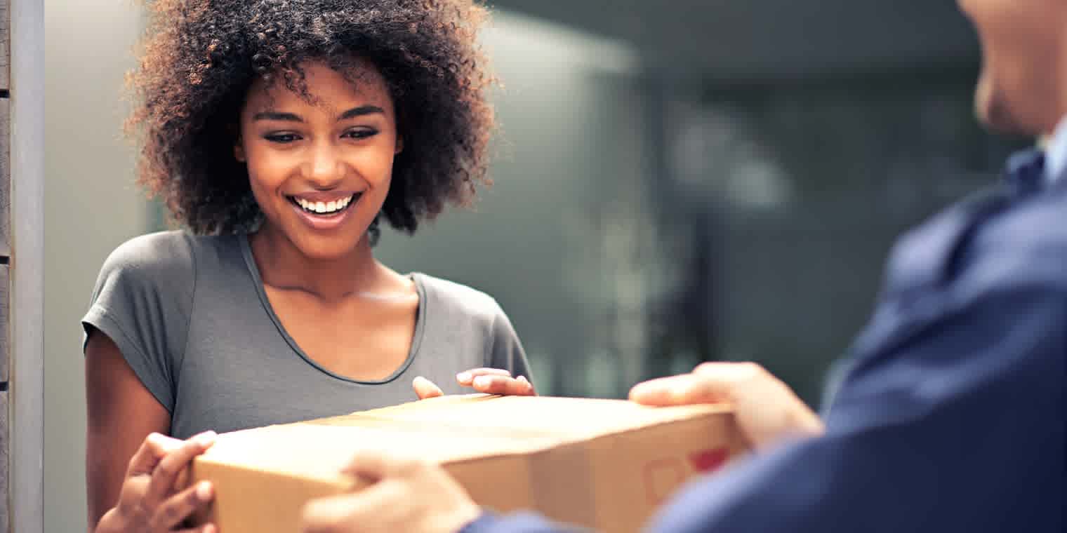 A smiling woman accepts delivery of a package from a delivery person.