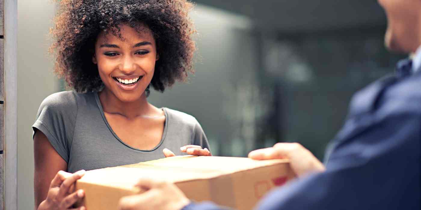 A smiling woman accepts delivery of a package from a delivery person. 