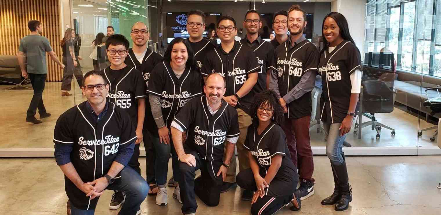12 members of the ServiceTitan team wearing matching baseball jerseys smile at the camera.