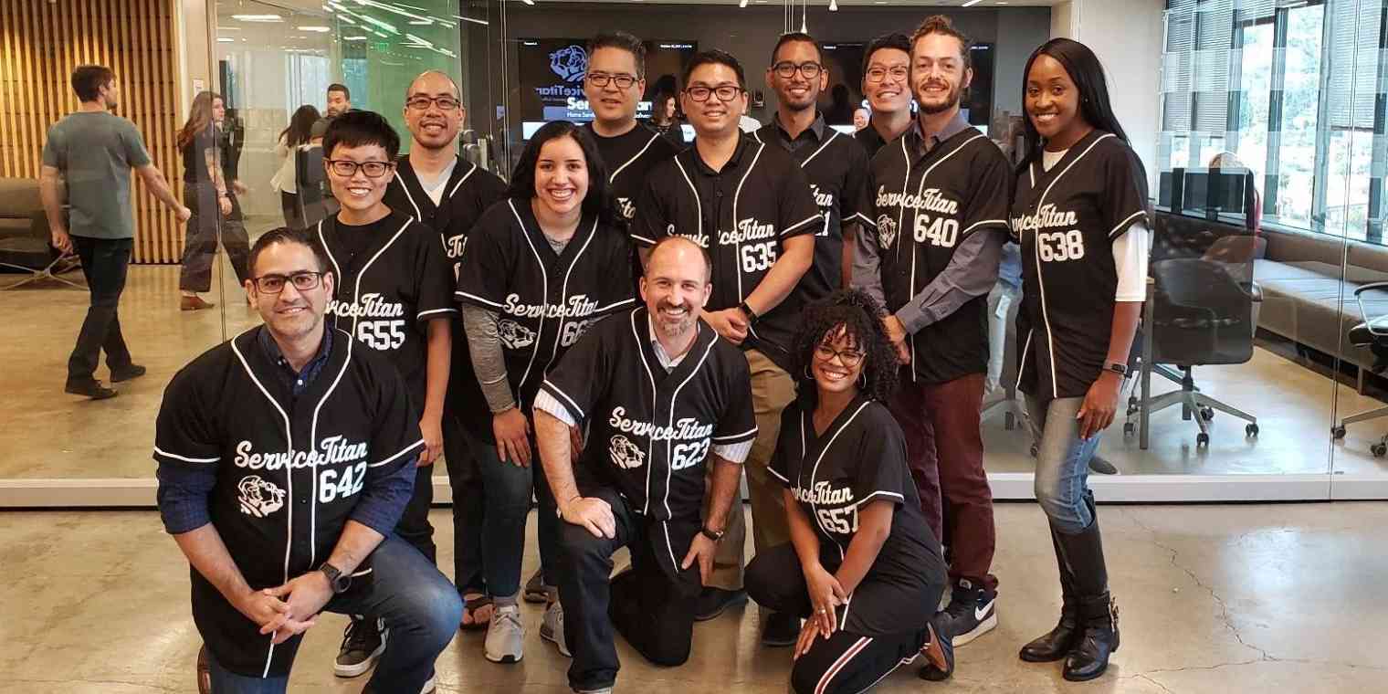 12 members of the ServiceTitan team wearing matching baseball jerseys smile at the camera.