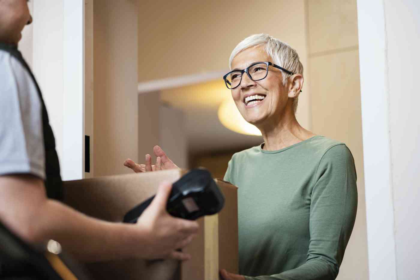 A senior woman accepts a package from a delivery person who is holding a scanning or payment device.