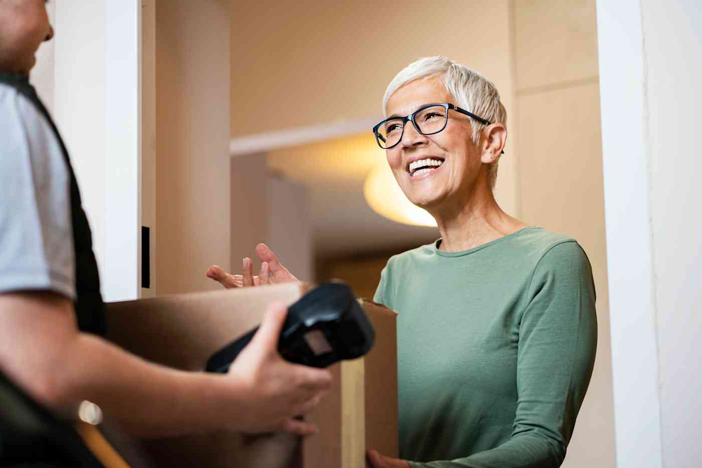 A senior woman accepts a package from a delivery person who is holding a scanning or payment device.