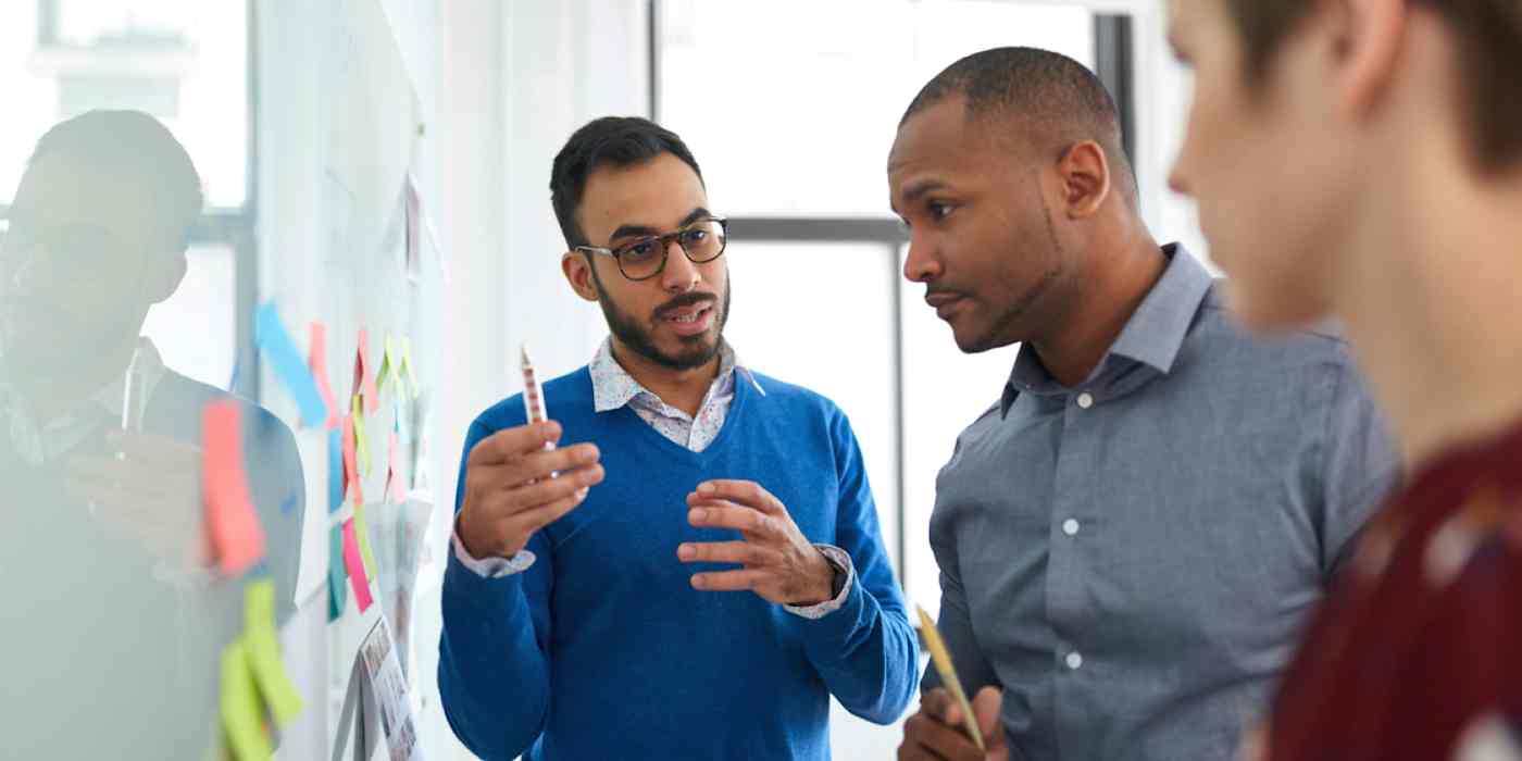 Hero image of three people looking at a whiteboard with Post-it notes on it