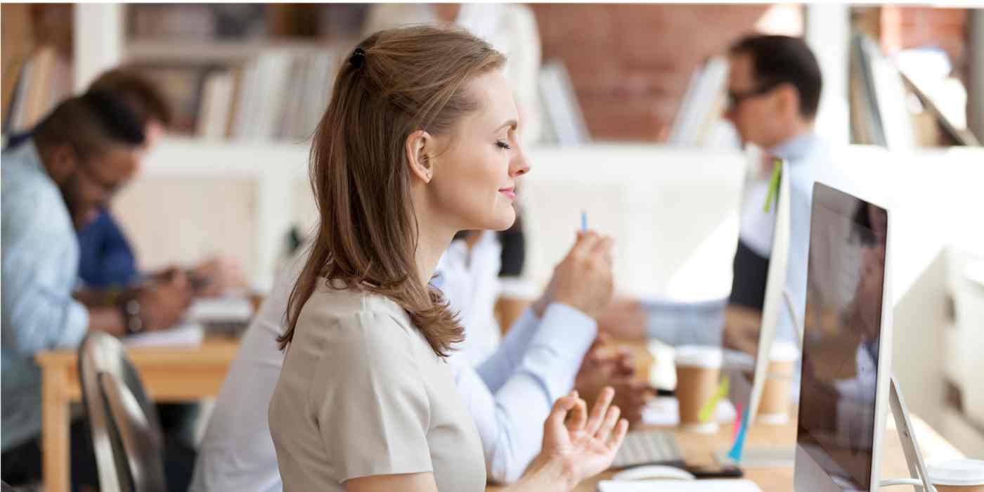 A hero image of a woman meditating at her desk