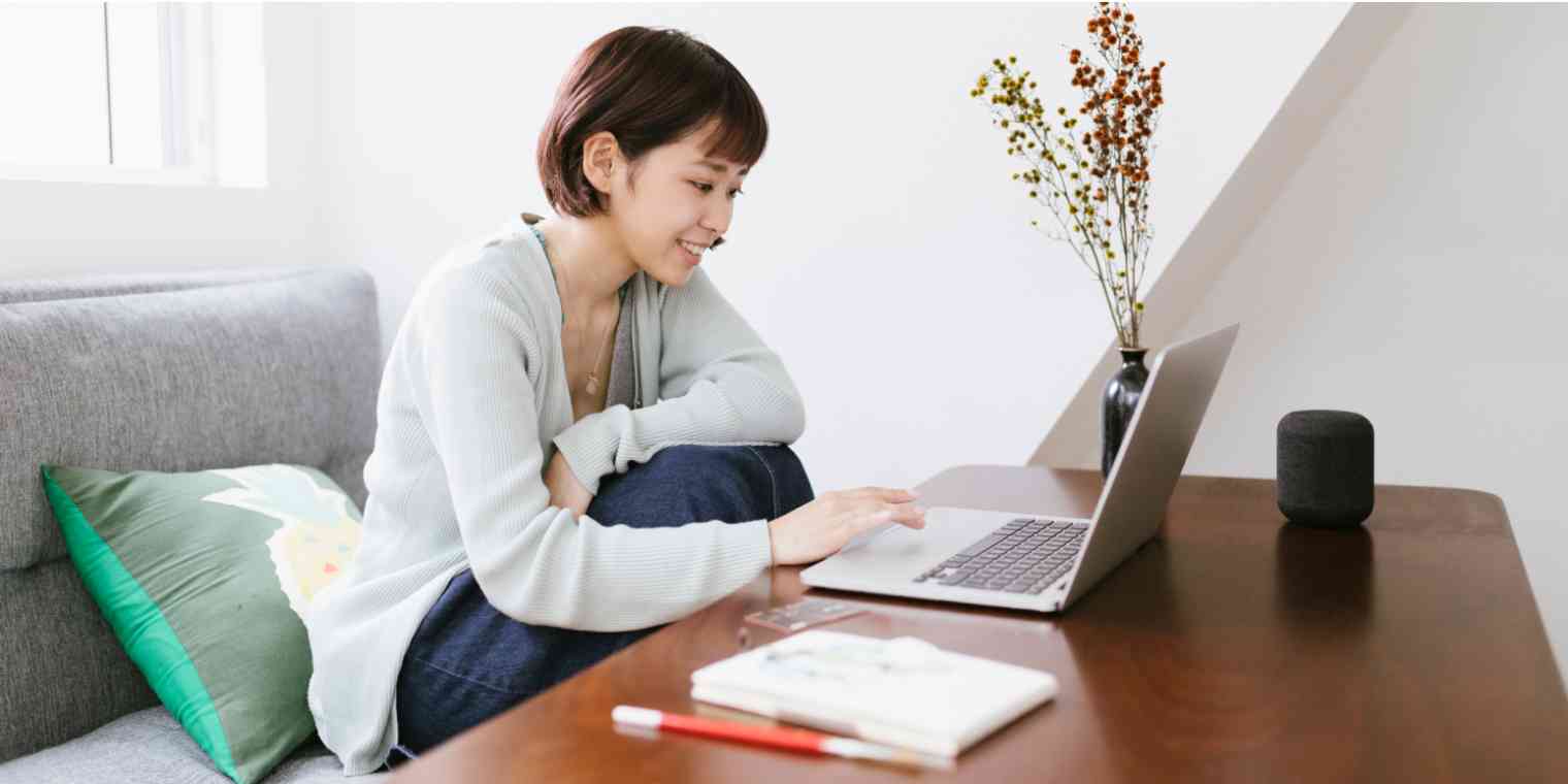 Hero image of a woman on a couch, with a table in front of her, looking at the computer and smiling
