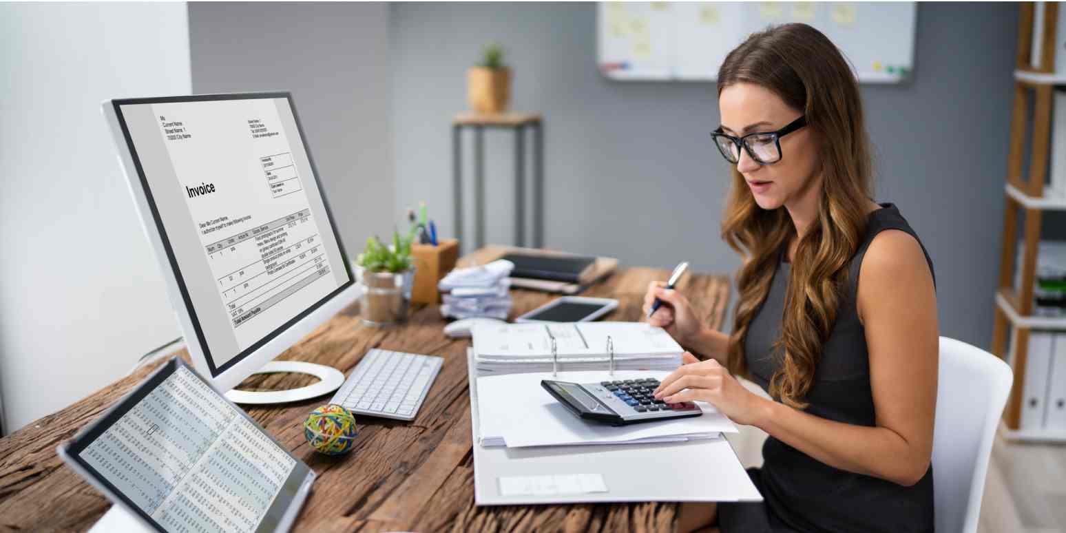 Hero image of a woman creating an invoice on a computer, with a calculator and binder
