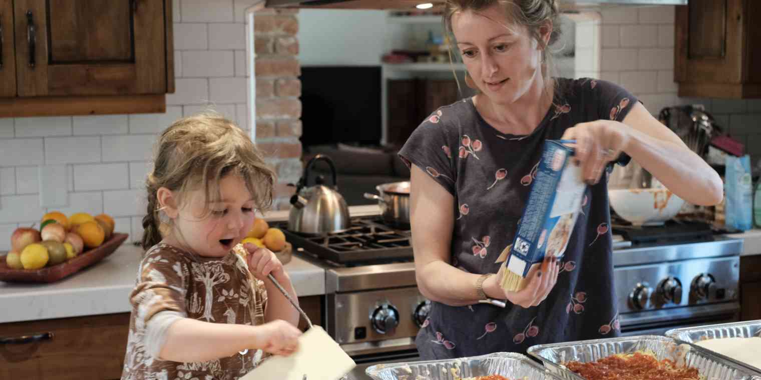 A hero image of a woman and young girl making lasagnas in a home kitchen