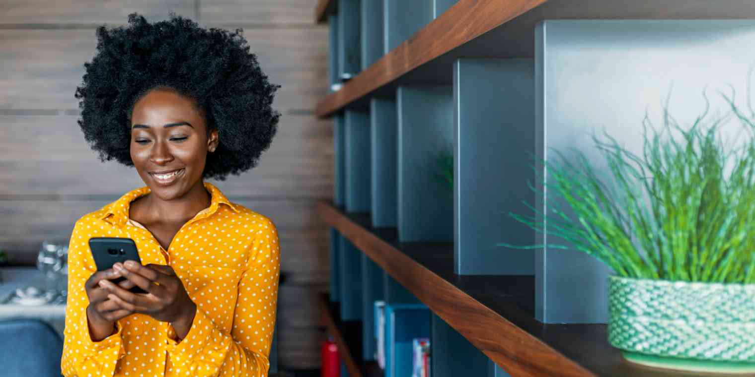 Hero image of a woman next to a bookshelf looking at her phone and smiling