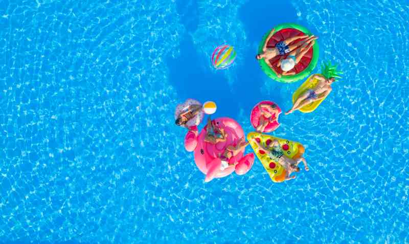 istock-00-pool Aerial view of a pool on a sunny day. People float on pool inflatables shaped like a flamingo, donut, pizza, pineapple, and watermelon.