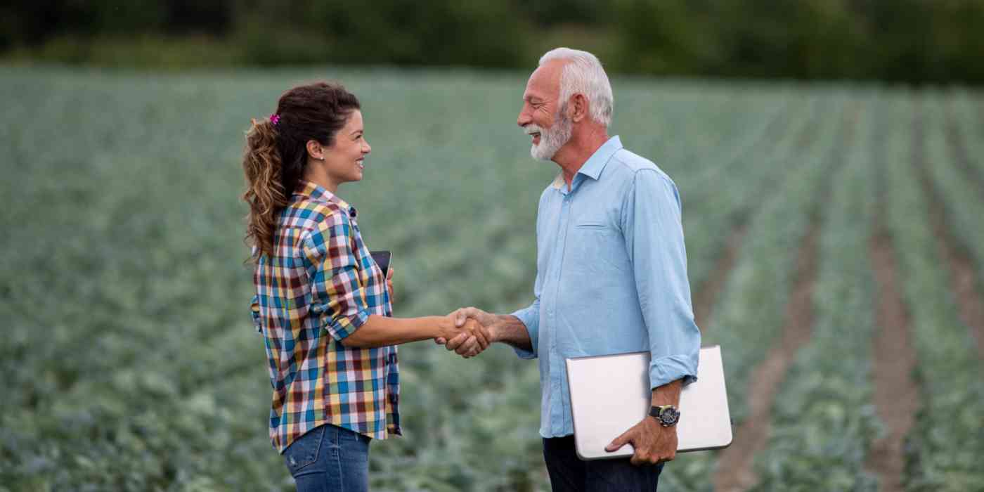 Hero image of a young woman and elderly man shaking hands in a field