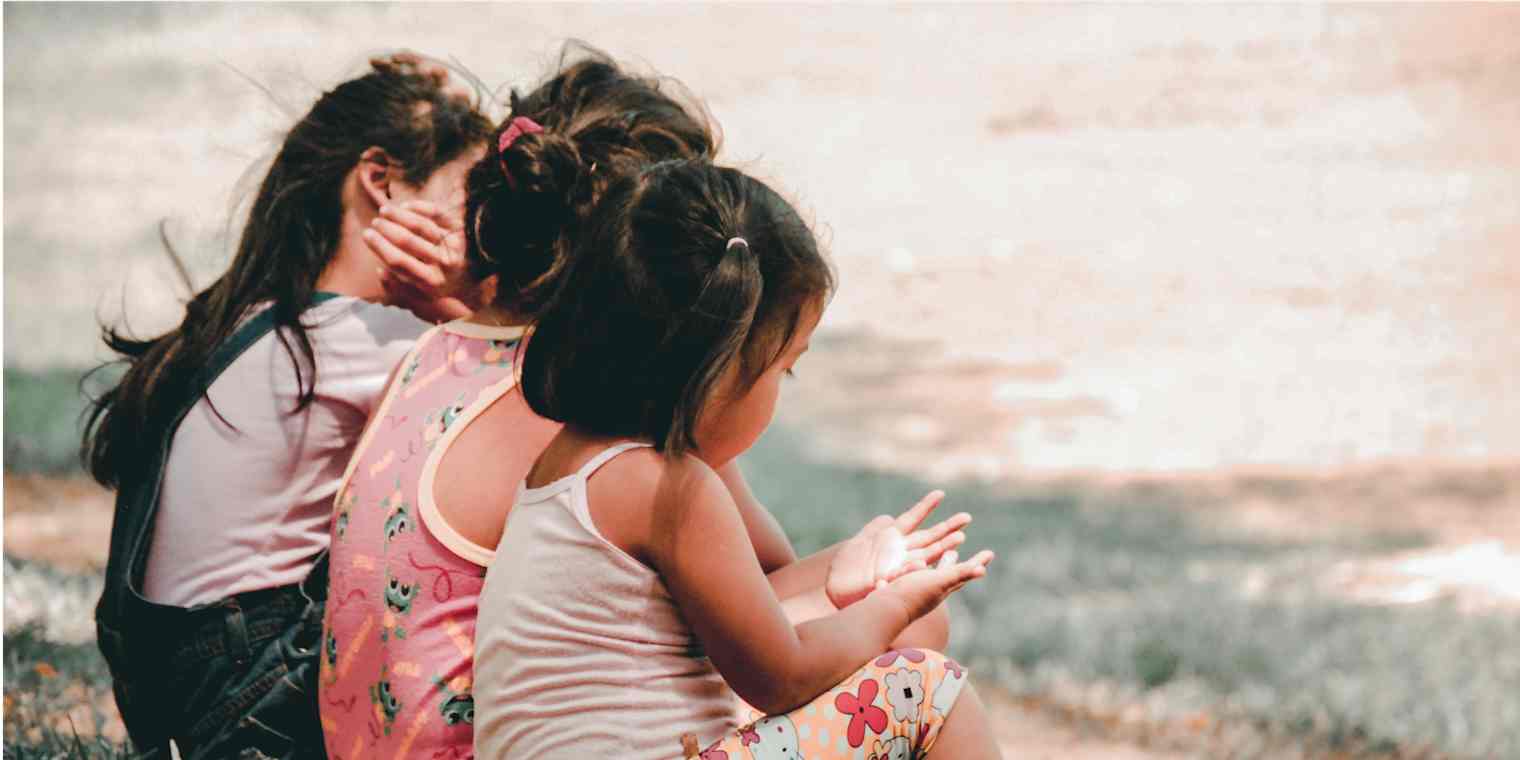 Hero image with three children sitting, looking at their hands (from the back)