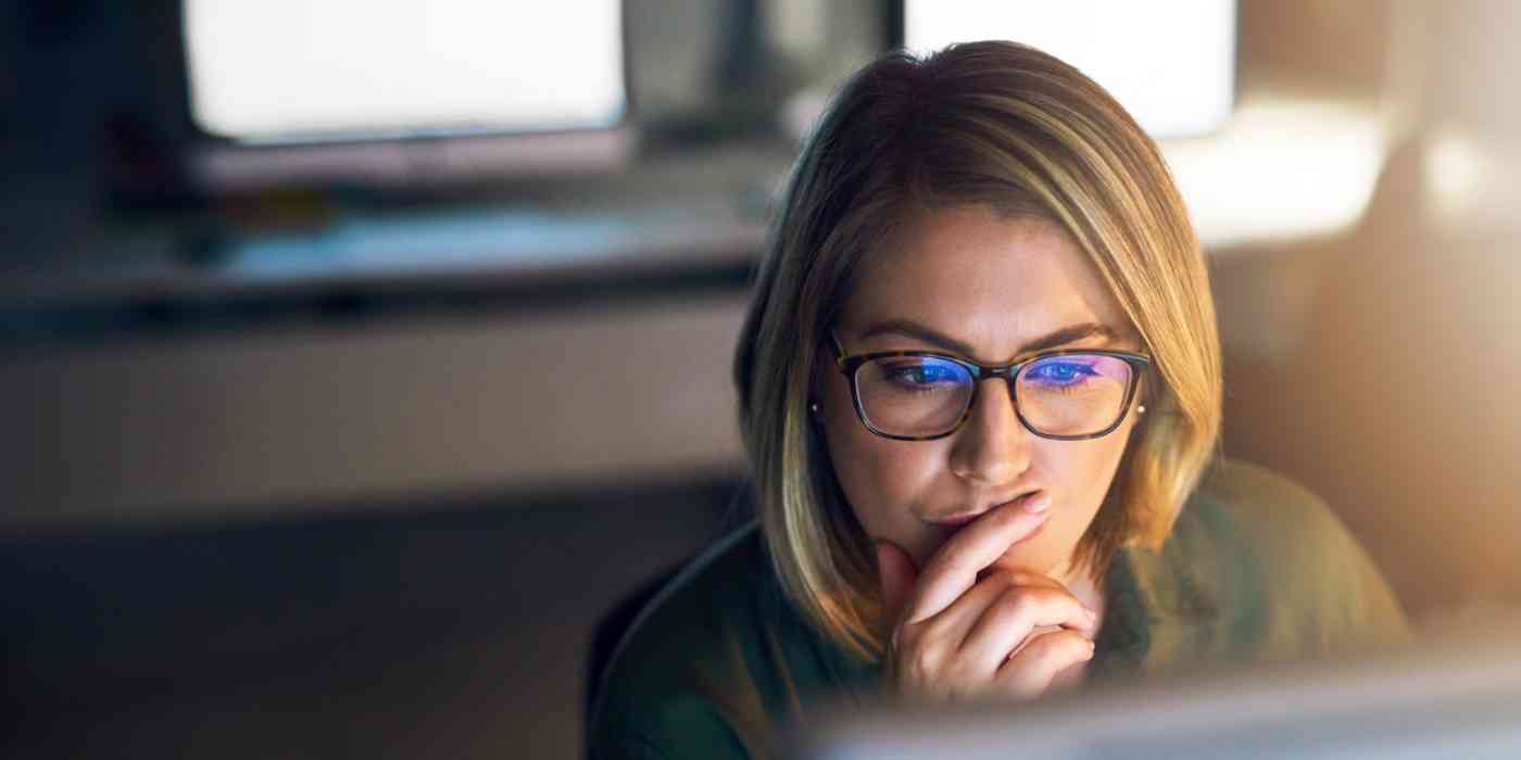 Screenshot of a woman looking at a computer with her finger over her mouth, thinking