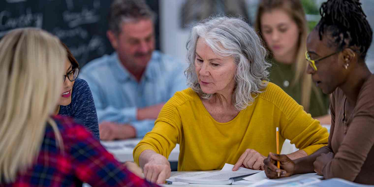 A group of adult students works from textbooks at a table.