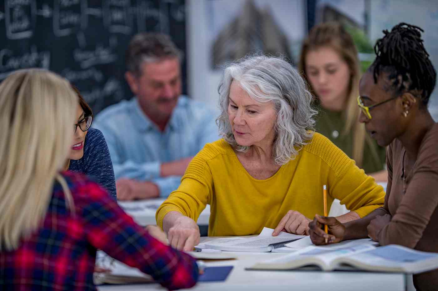 A group of adult students works from textbooks at a table. 