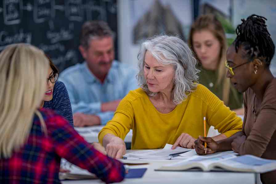 A group of adult students works from textbooks at a table. 