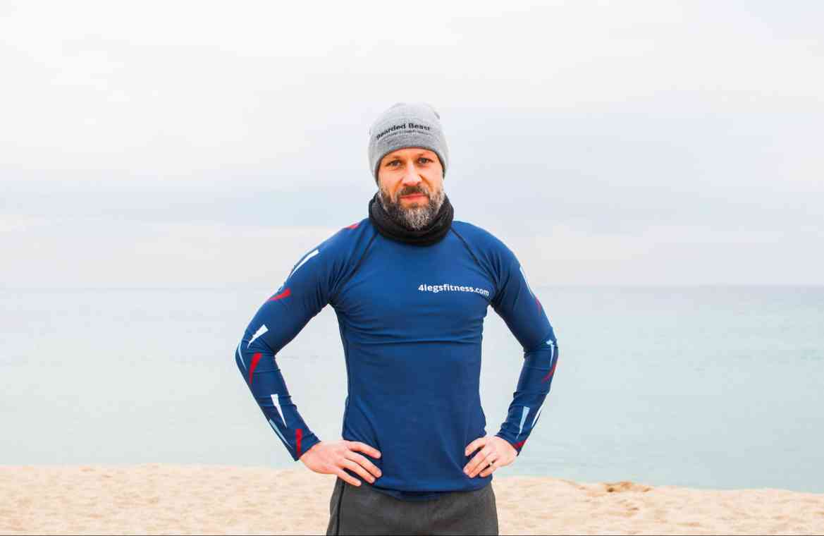 A man in workout gear and a hat stands on a beach.