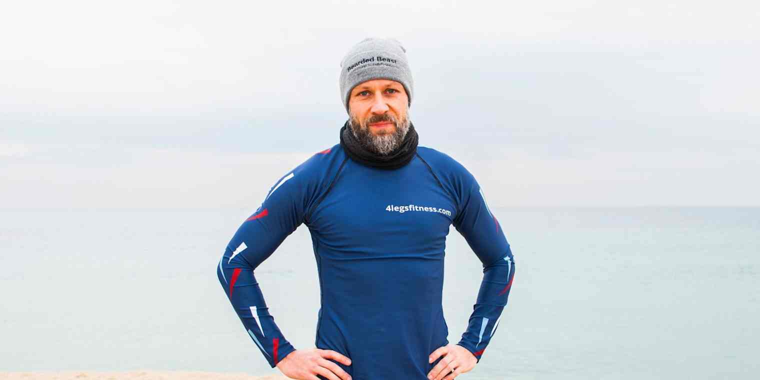 A man in workout gear and a hat stands on a beach.