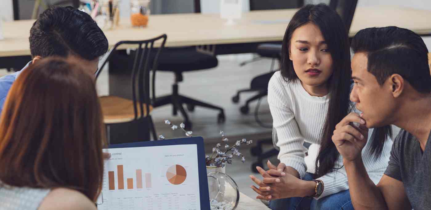 Hero image of four people sitting around a computer with charts and graphs on it