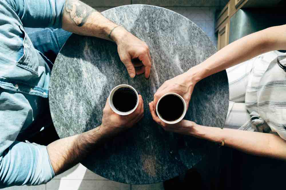 Two sets of hands across a table from each other holding cups of coffee