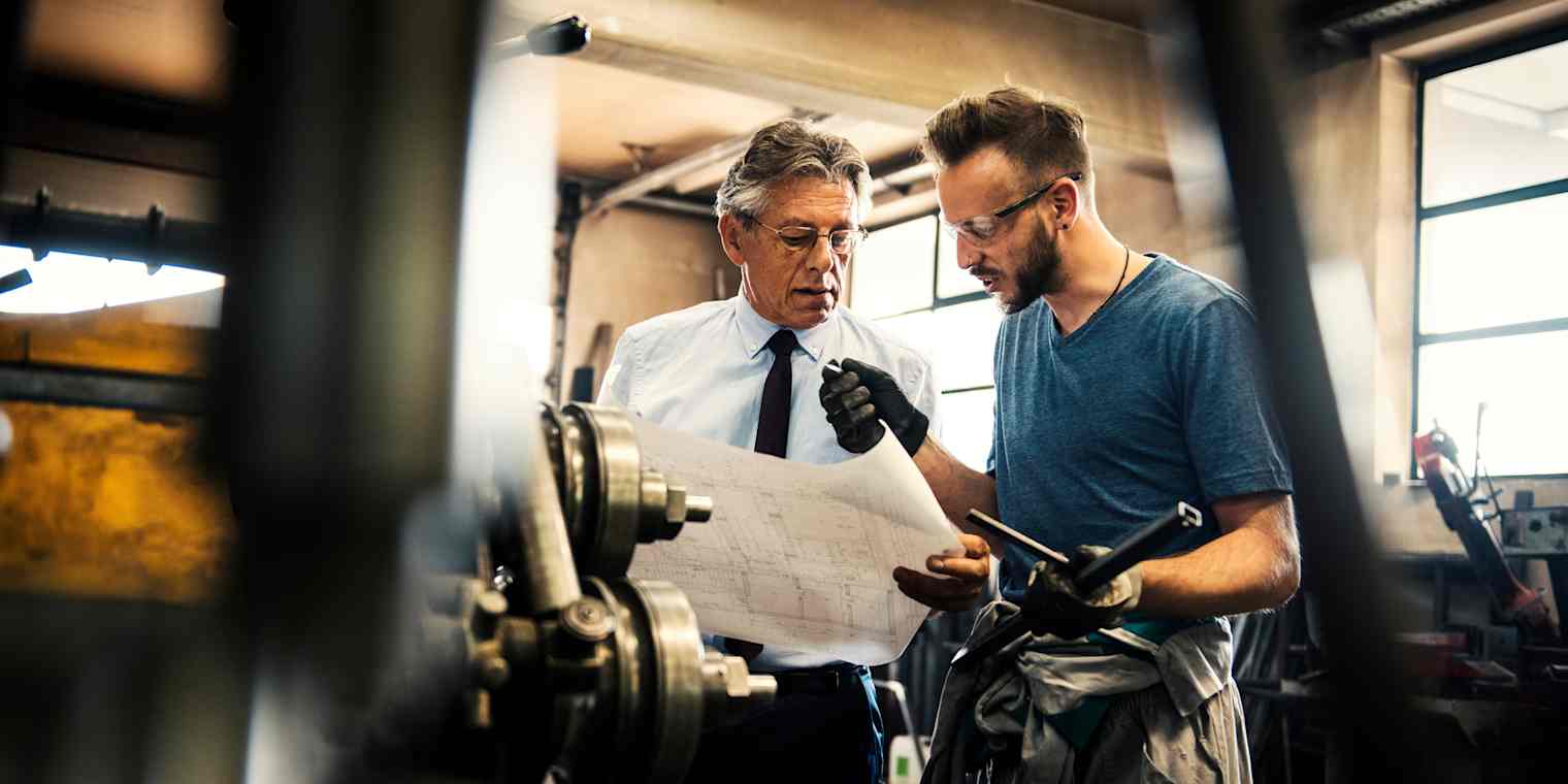 Two men review plans in a workroom.