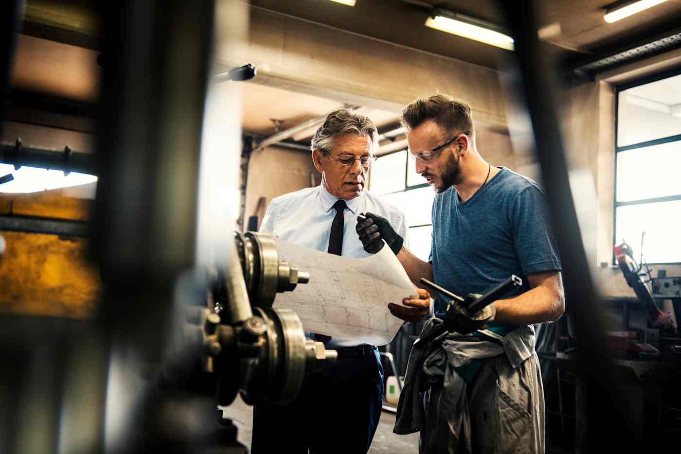 Two men review plans in a workroom.