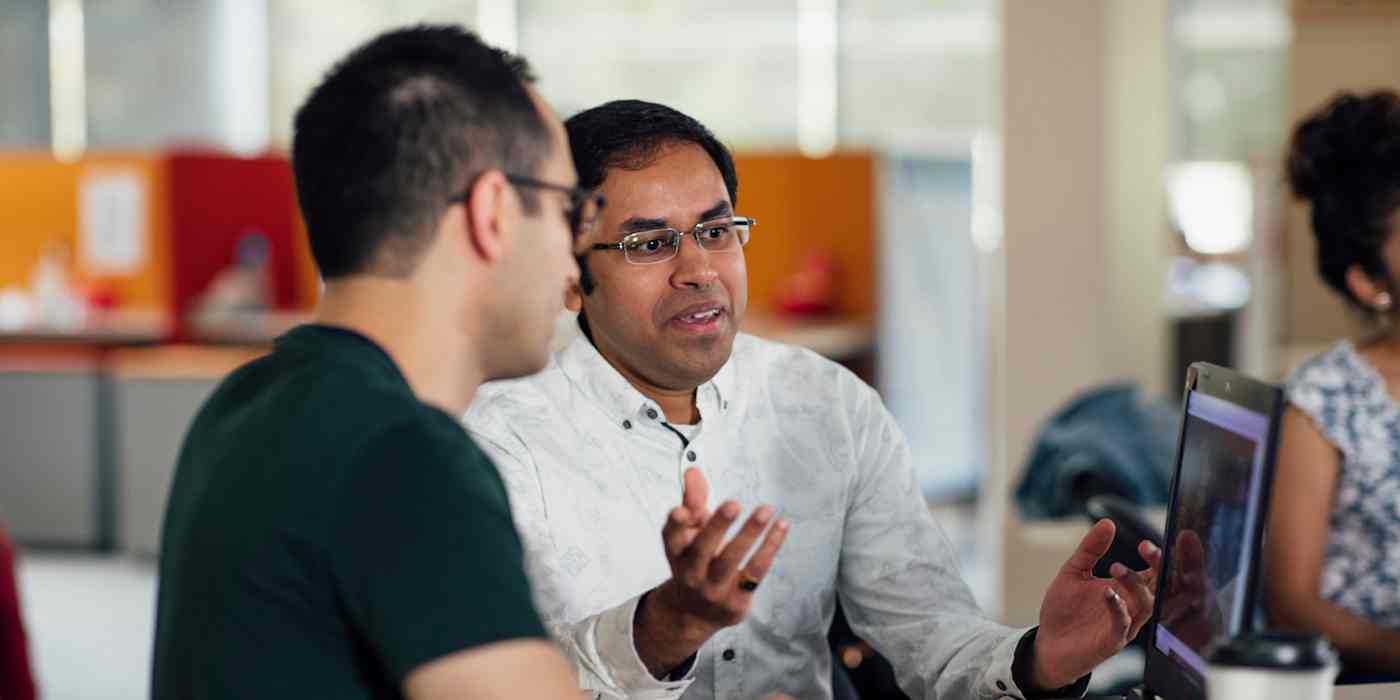 Hero image of two people talking in an open office in front of a computer