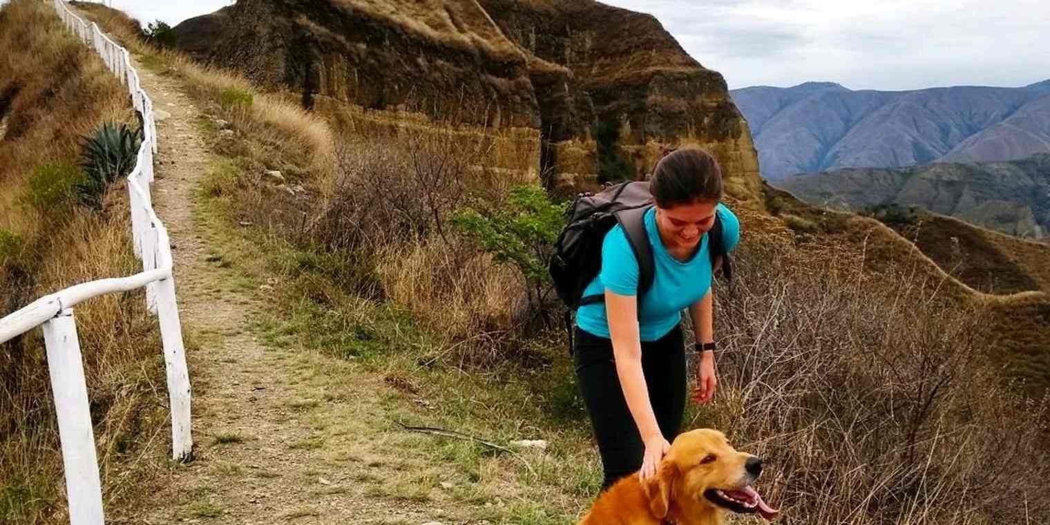 A woman petting a Golden Retriever dog on a mountain trail.
