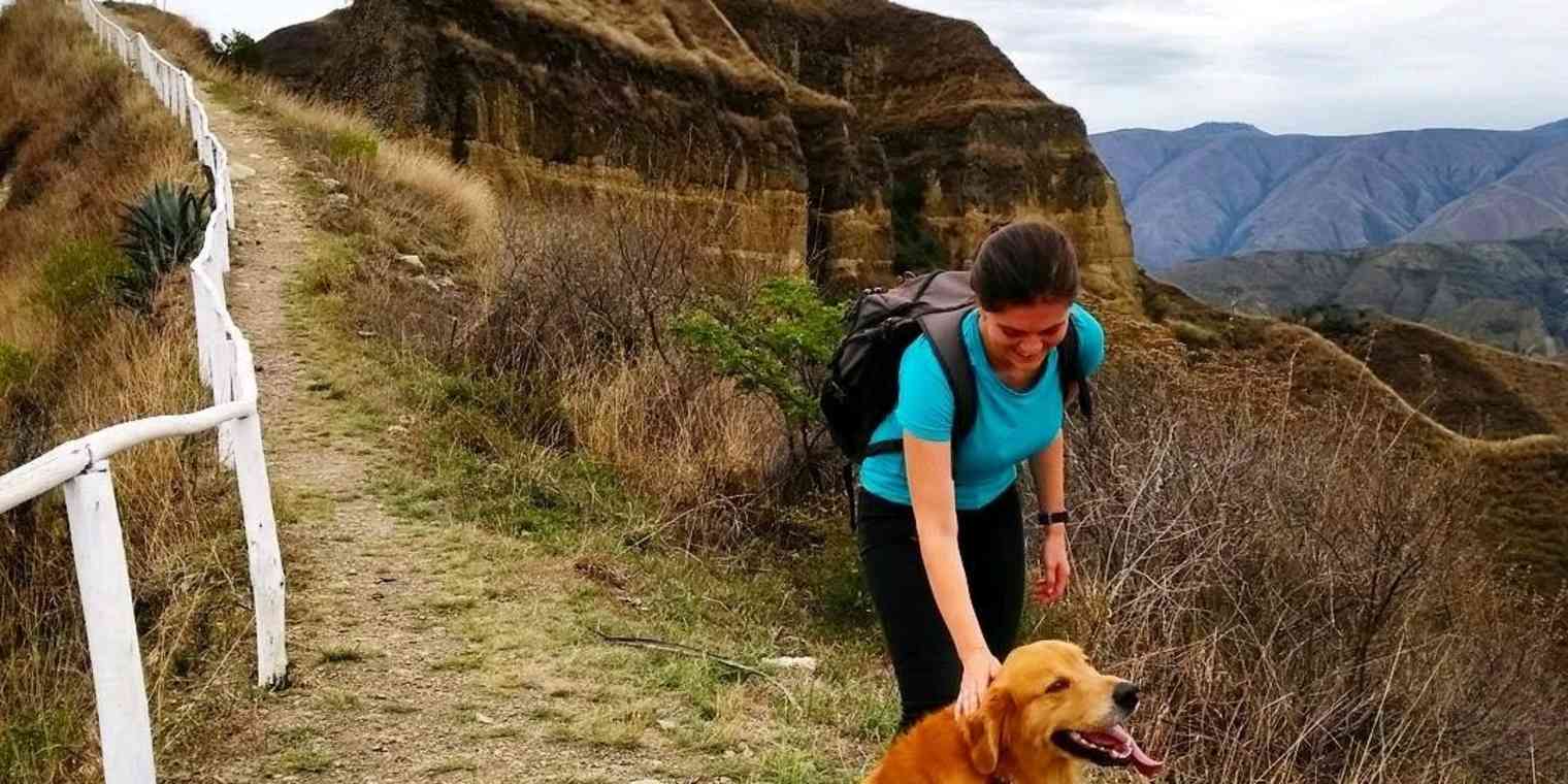 A woman petting a Golden Retriever dog on a mountain trail.