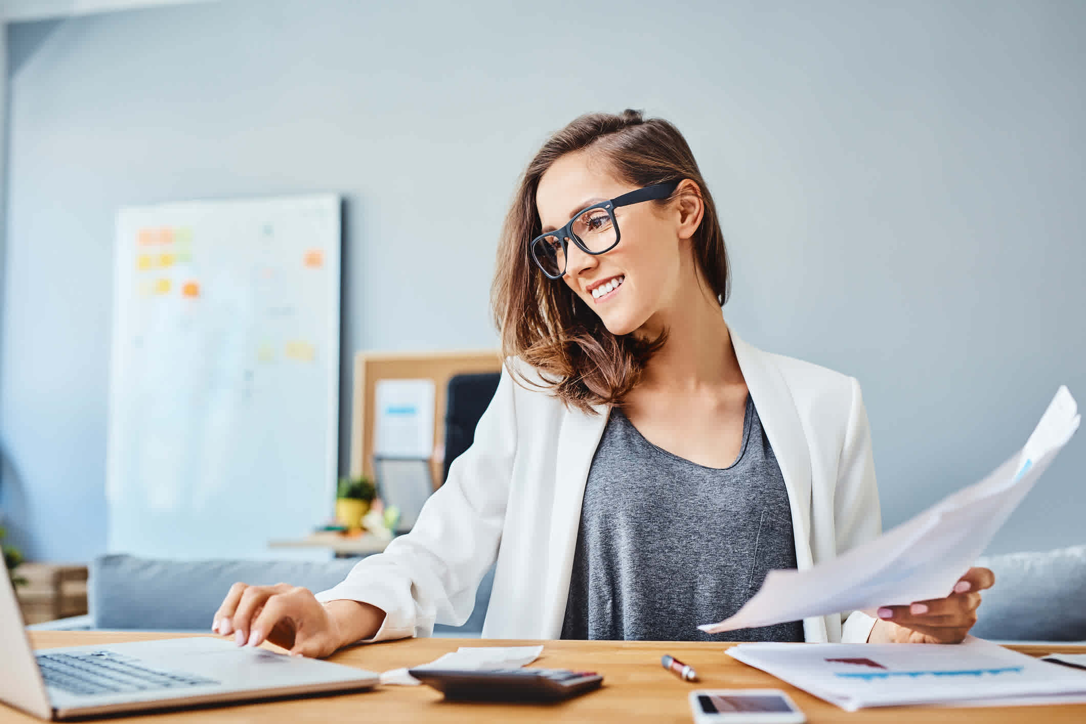 A woman works with a laptop, calculator, and holds papers.