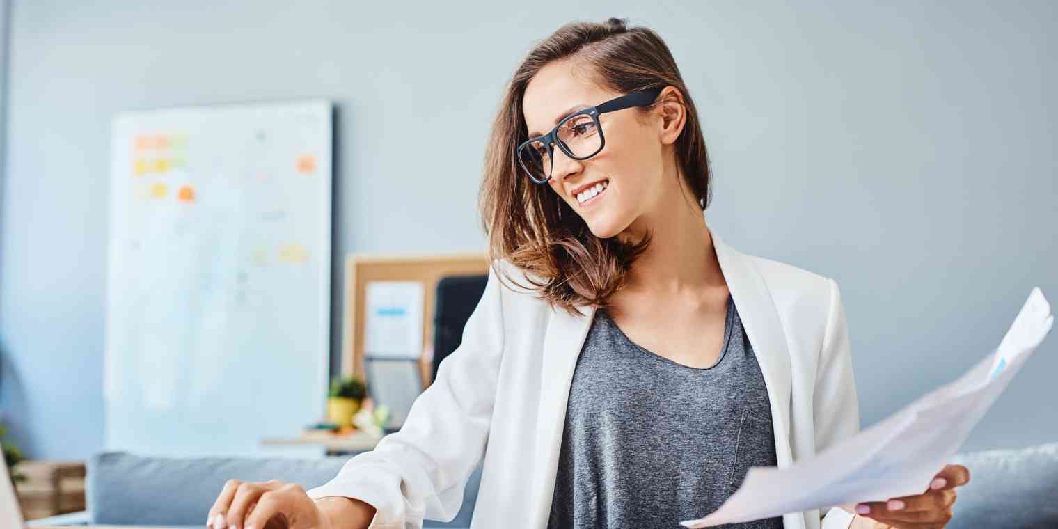 A woman works with a laptop, calculator, and holds papers.