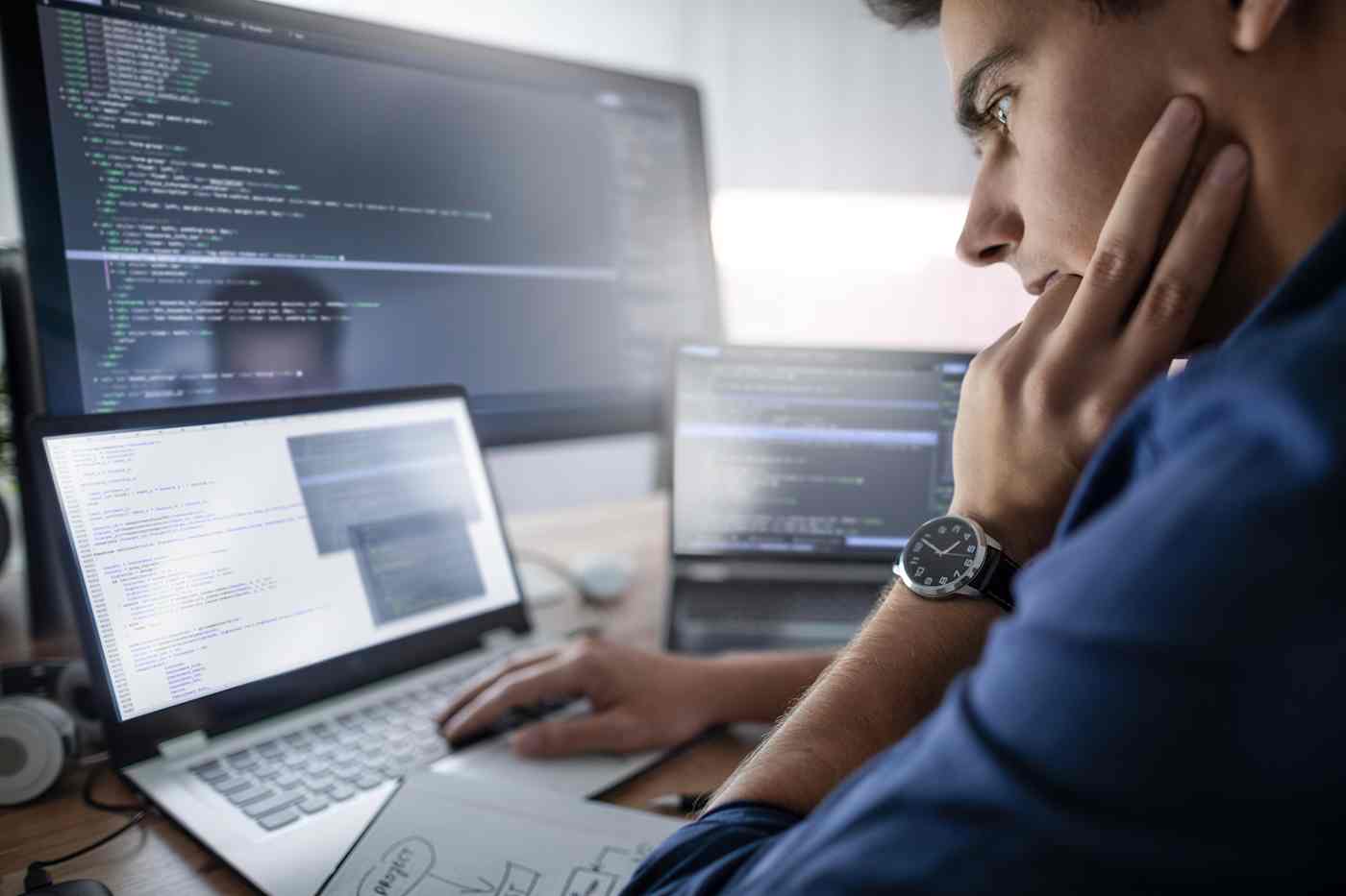 A man sits in front of computer screens and a laptop.