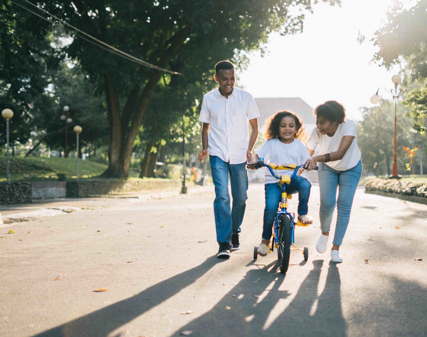 Image of child learning to ride a bike with the help of adults