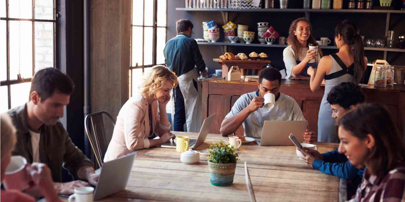 A lot of people sitting together at a coffee shop, some of them working