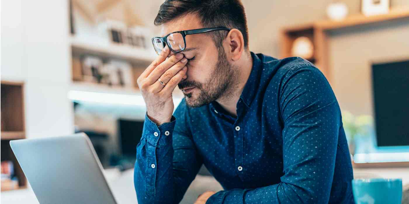 Hero of a man looking frustrated in front of a computer, with his hand on his face