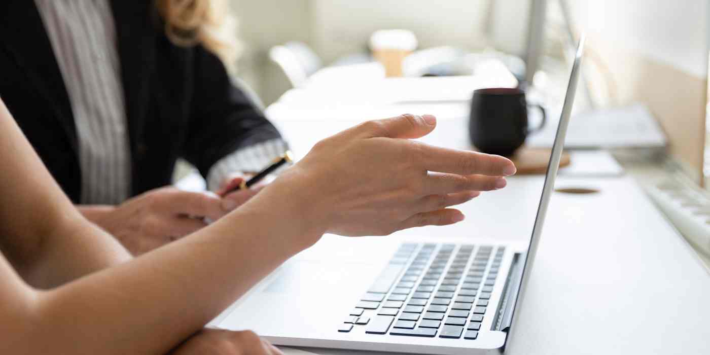 Hero image of a hand pointing at a computer (two people are sitting at the computer)