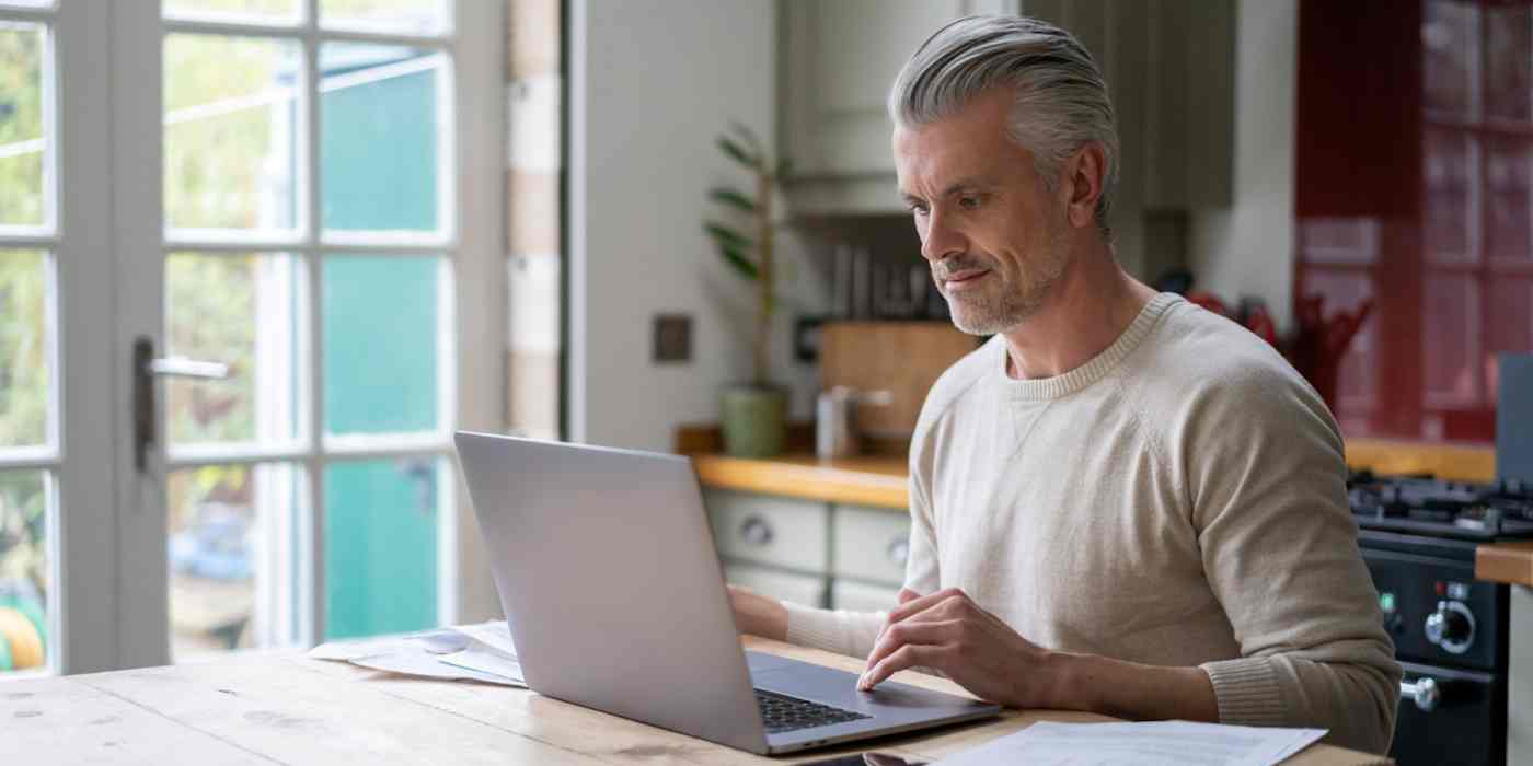 Hero image of a man with gray hair sitting at a computer in a kitchen