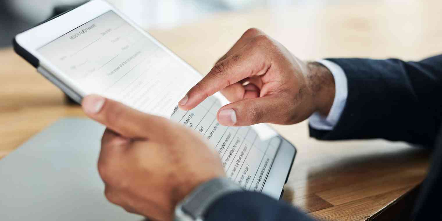 A close-up of the hands of a person wearing a shirt and blazer filling out an online form on a tablet.