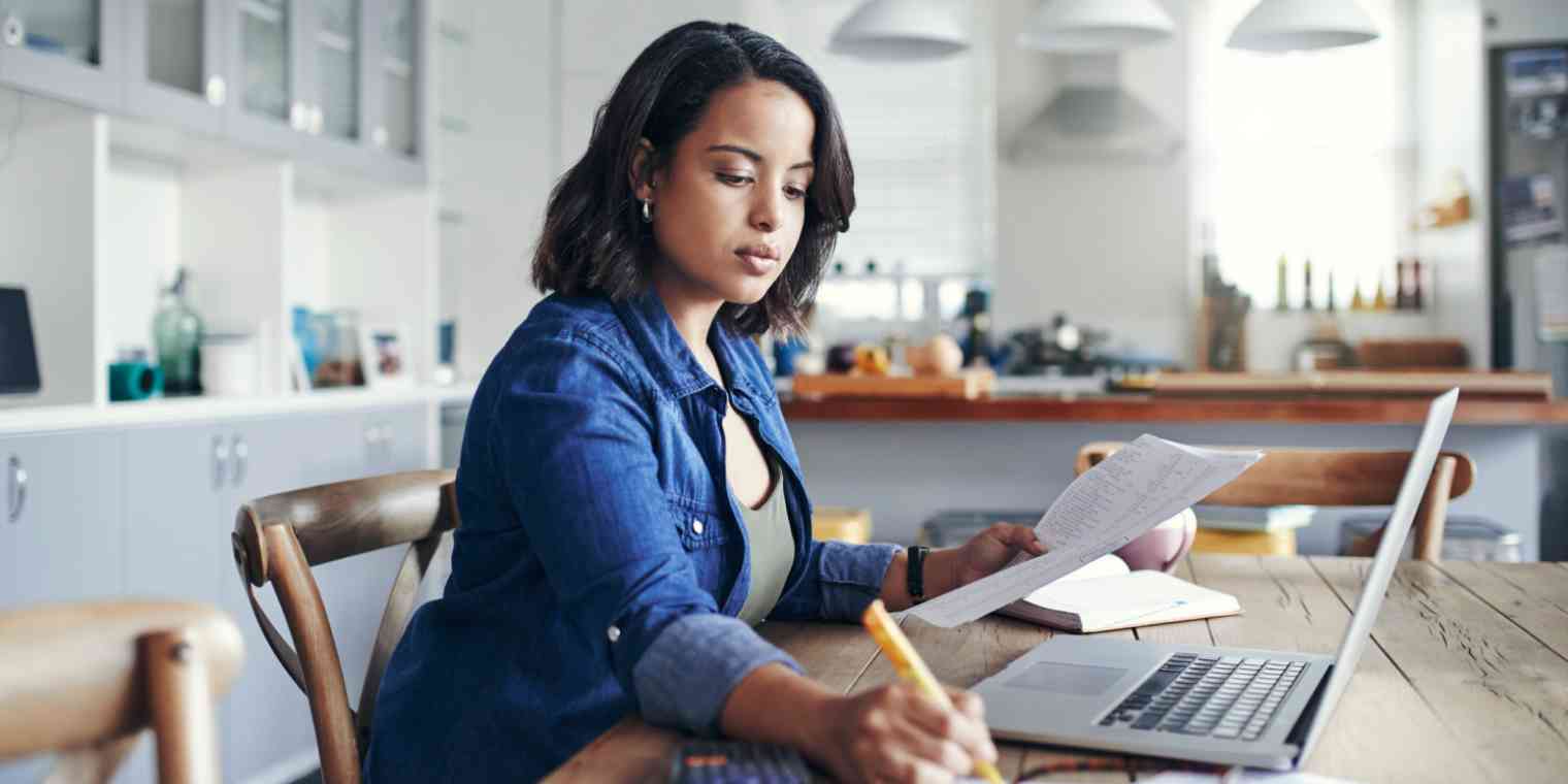 Hero image of a woman in front of a computer with papers in one hand and using a highlighter with the other