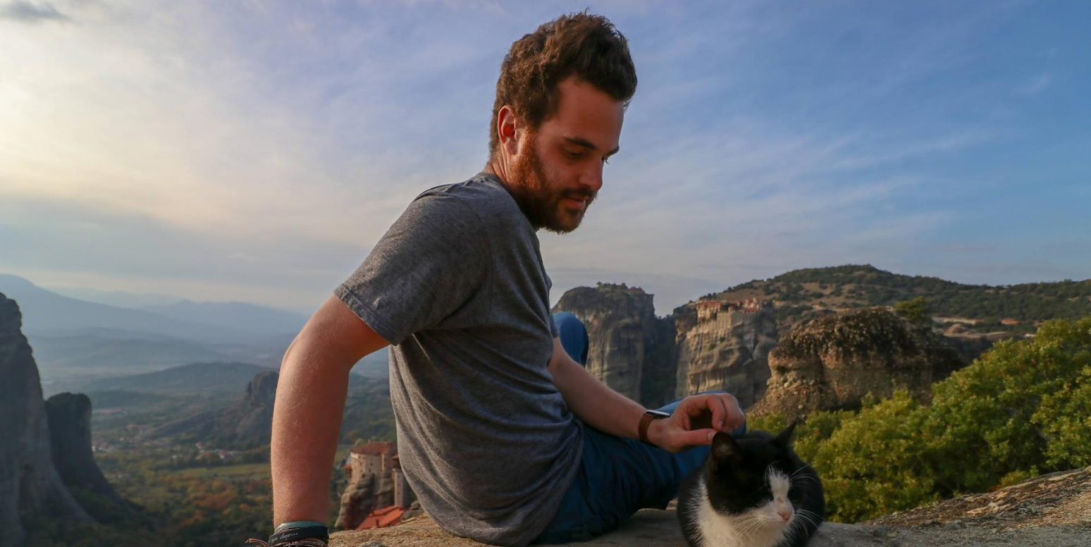 Hero image of a man sitting at the top of a mountain with a cat