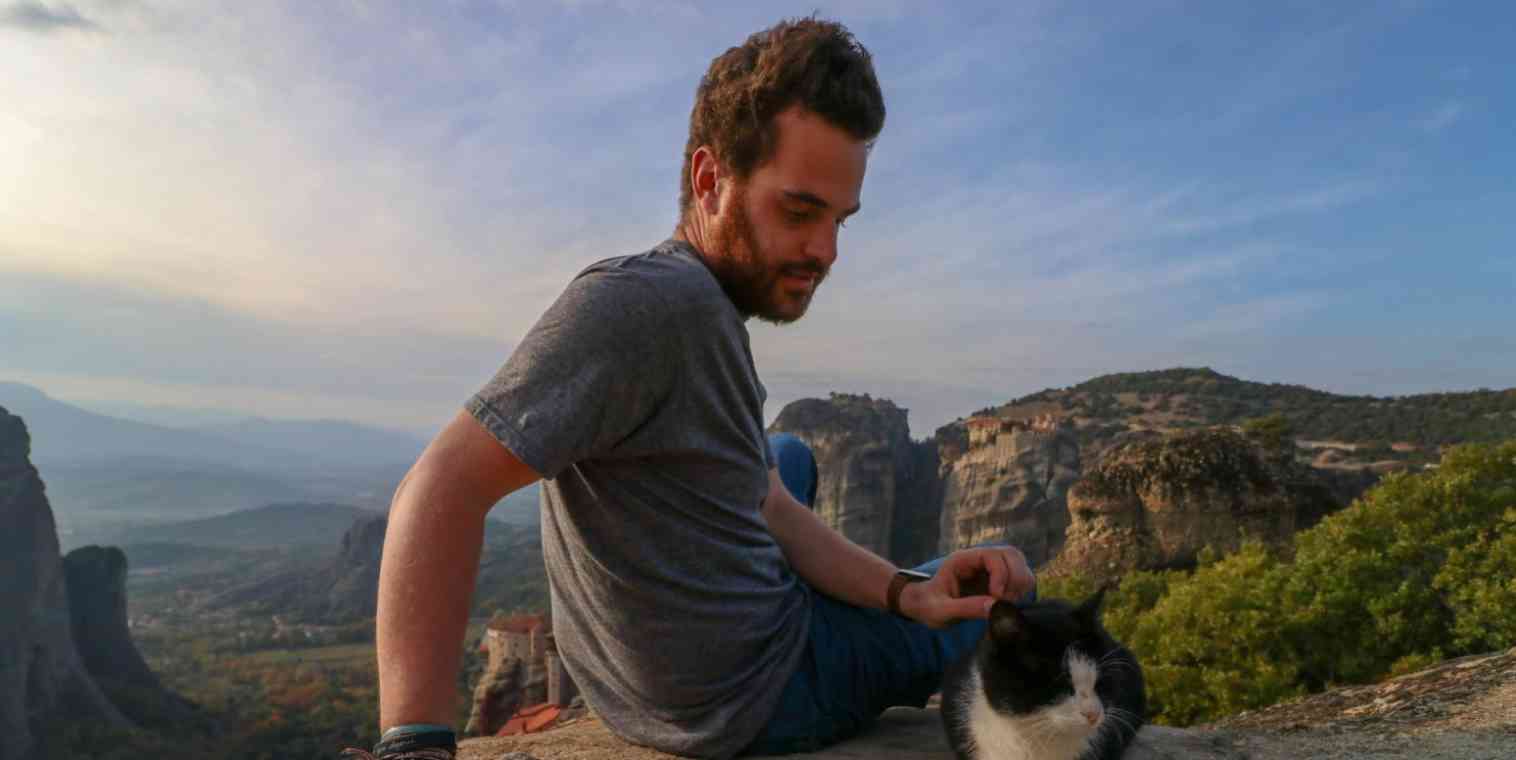 Hero image of a man sitting at the top of a mountain with a cat