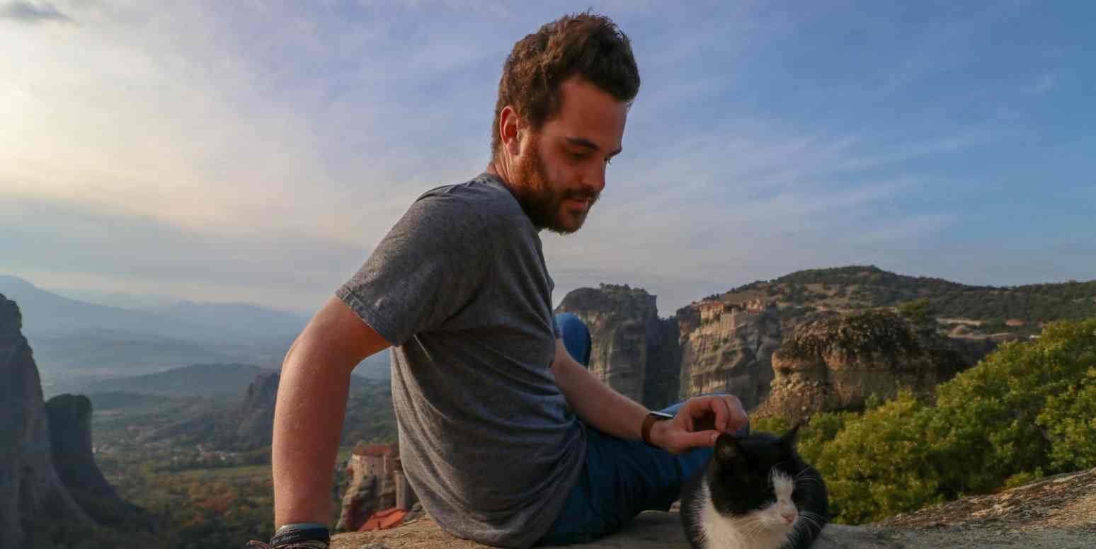 Hero image of a man sitting at the top of a mountain with a cat