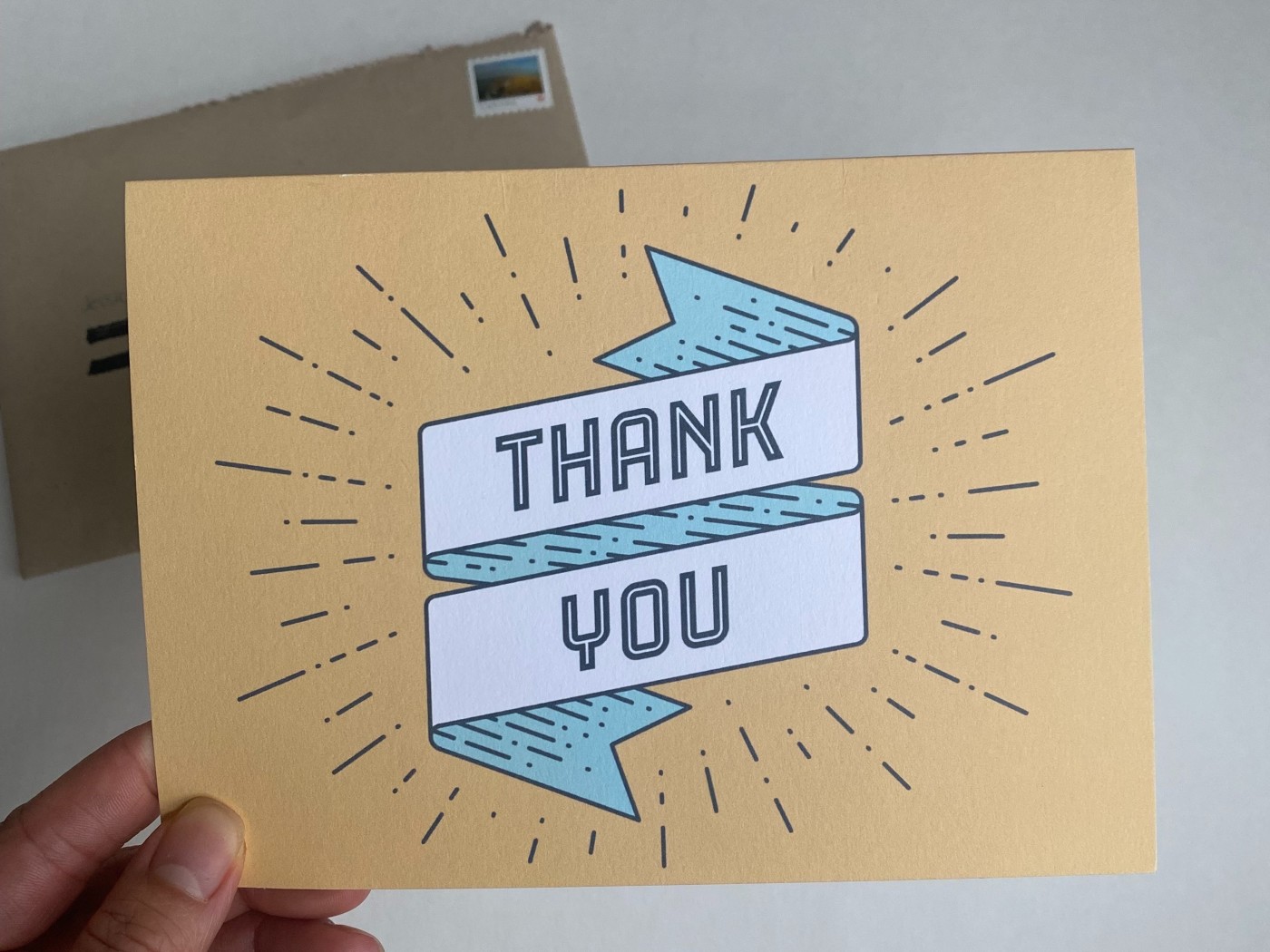 Front of a card from Cardly. There's an illustrated banned flowing vertically in the center with the words "thank you" in the center of the banner. There are thin black lines bursting out around the banner.