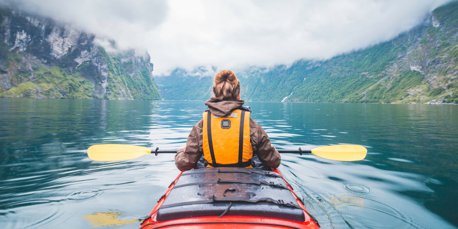 Hero image of a woman kayaking down a river between mountains