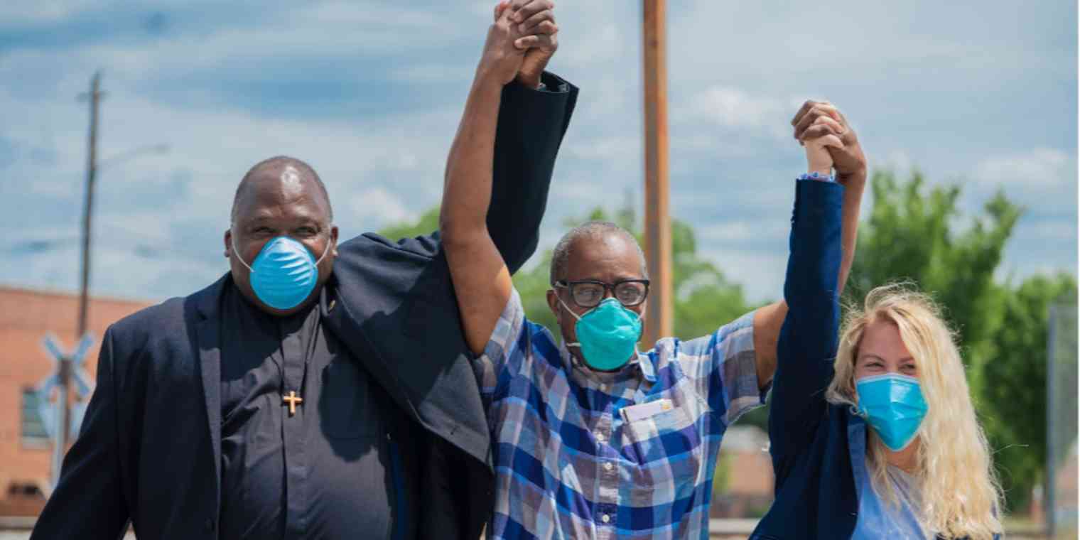 Three people with their hands linked and raised. They are celebrating the release from prison of the man in the middle, who was wrongfully imprisoned for more than 40 years.