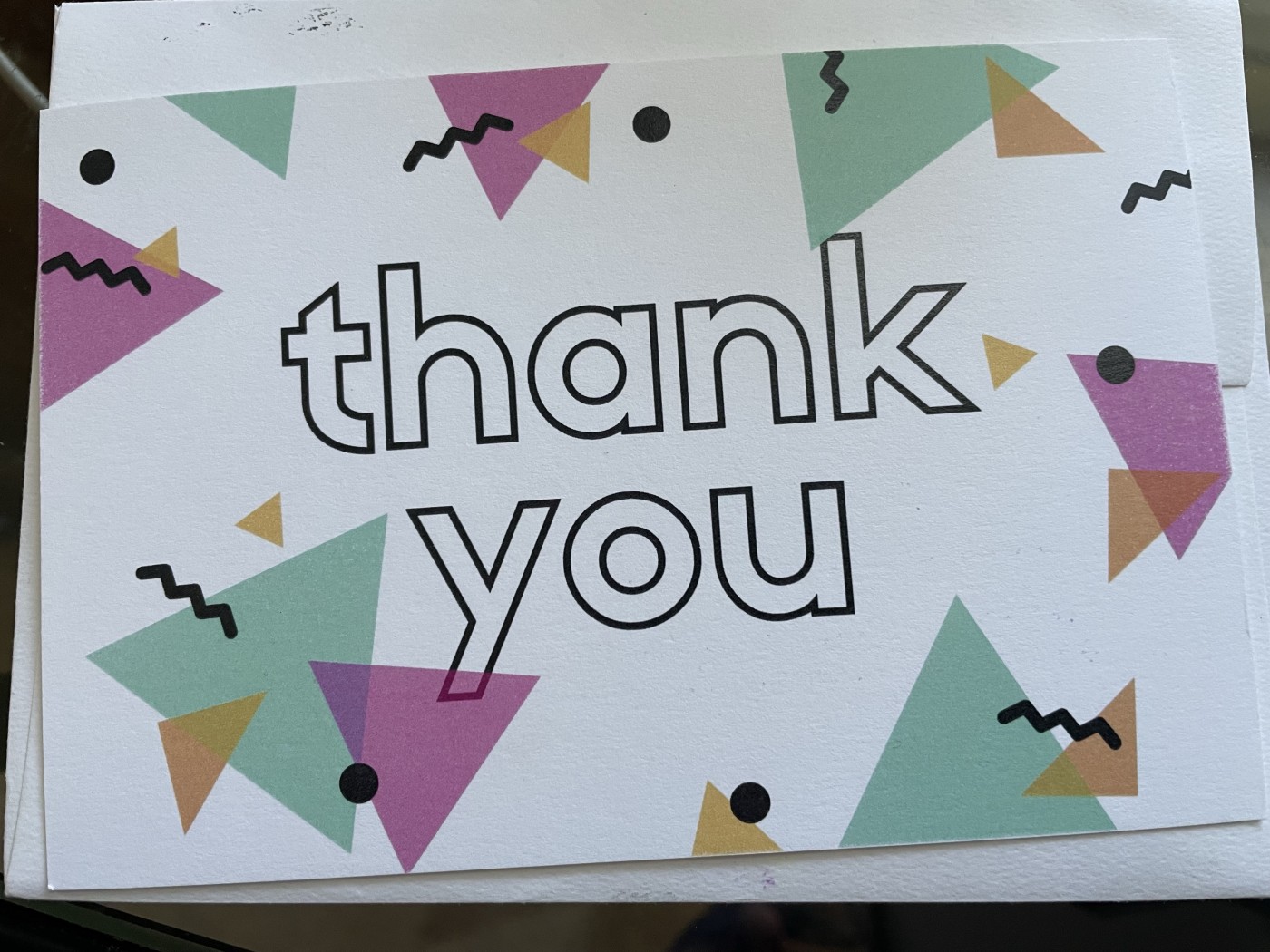 Front of a card from Handwrite with "thank you" printed in hollow block letters. The words are surrounded by pink, aqua, and orange triangles with black squiggles and dots.