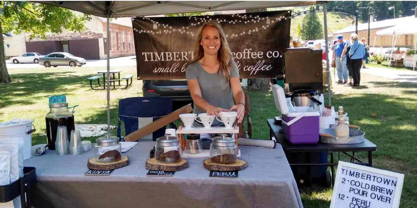 A hero image of the owner of Timbertown Coffee under a tent, with her coffees in front of her