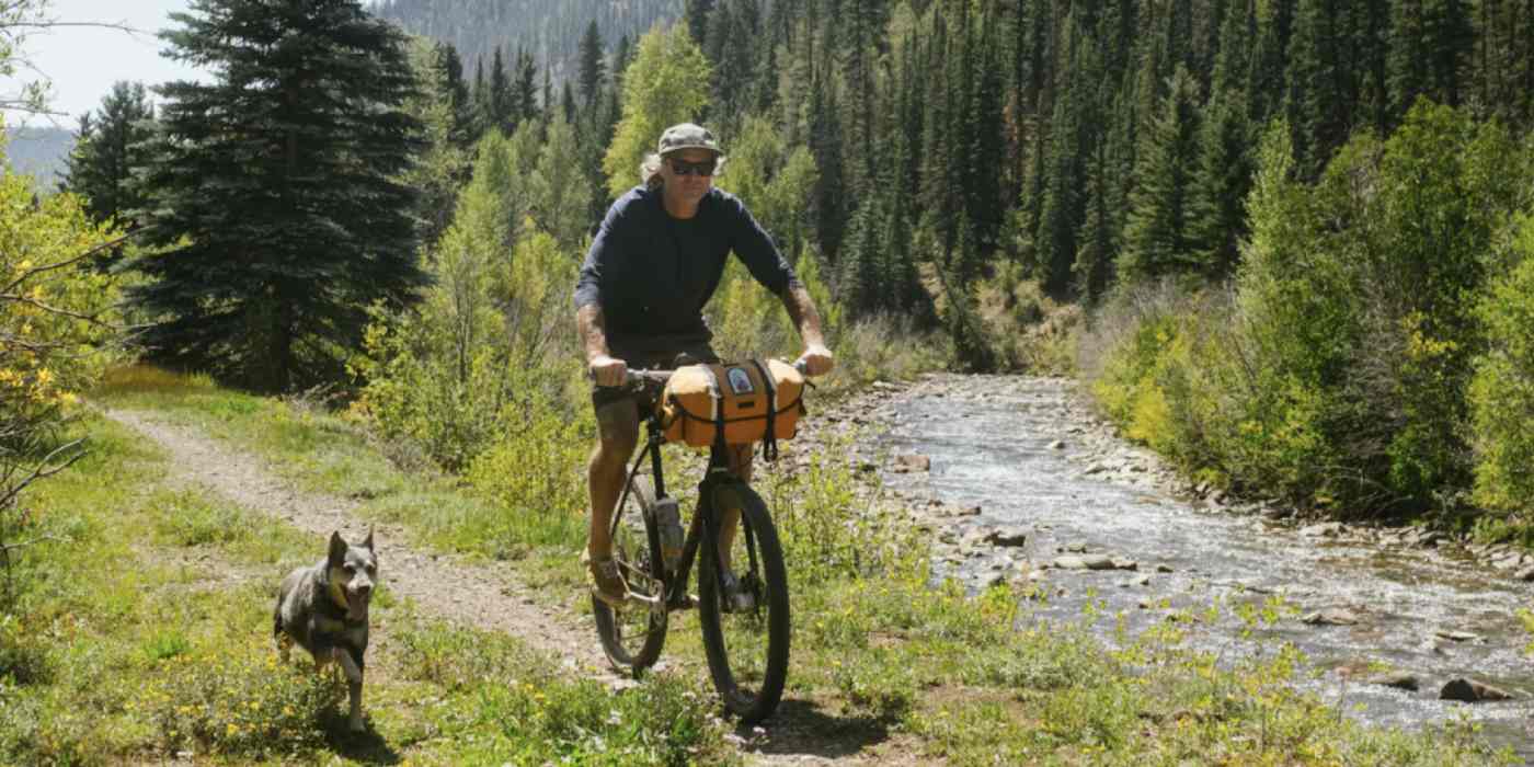 Hero image of a man riding a bike with a dog running alongside him