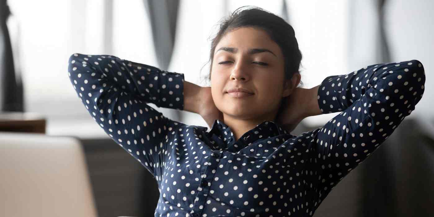 Hero image of a woman leaning back in a chair with her arms behind her head and her eyes closed