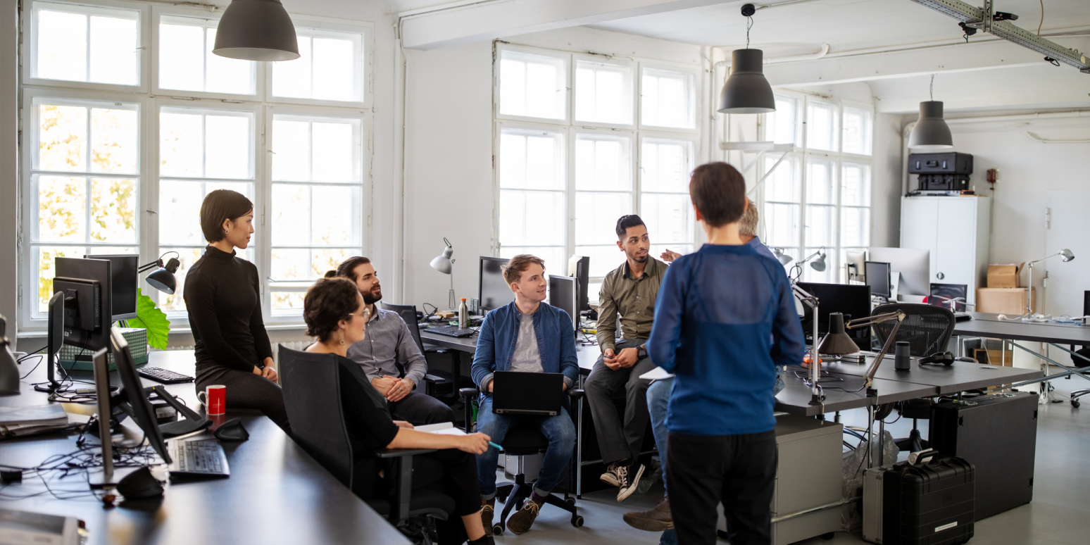 Hero image of a group of people chatting in a modern open office