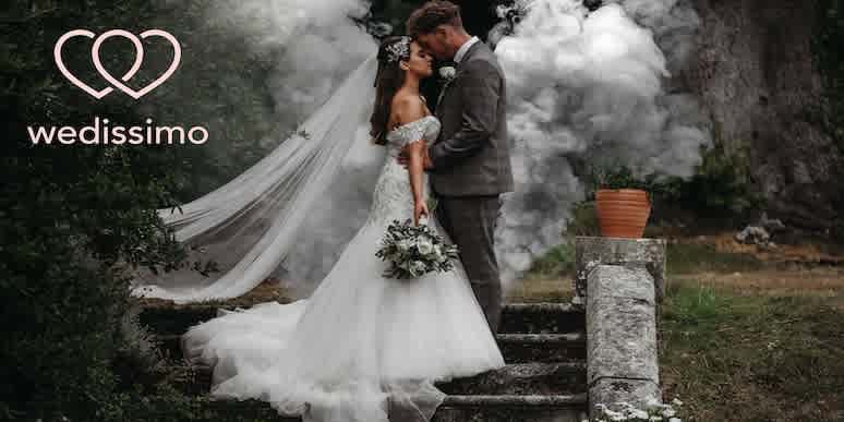 Professional photo of a brown-haired bride in a white wedding dress face-to-face with the groom in a gray suit and the Wedissimo logo in the upper-right corner.